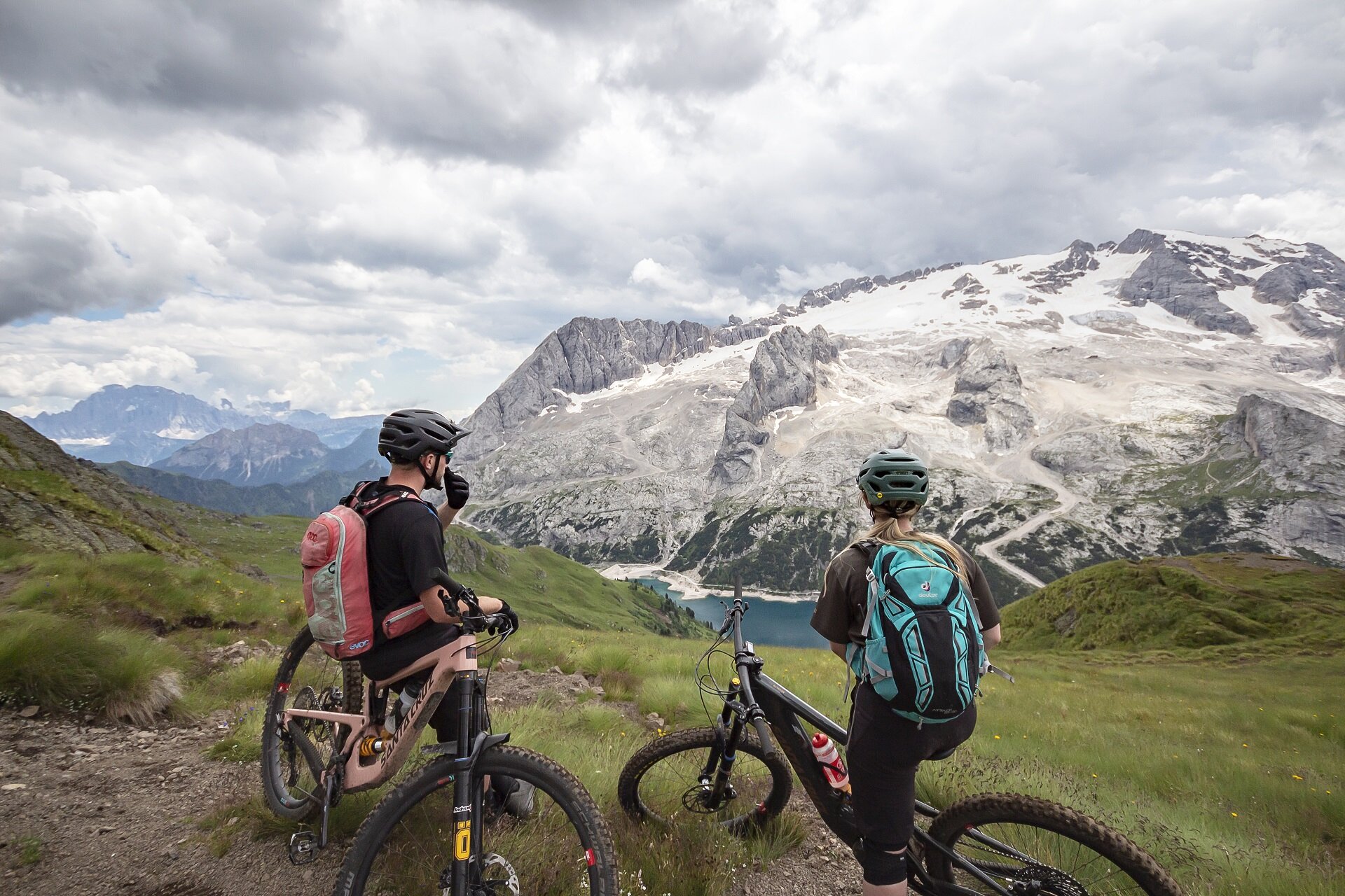 Persone che vanno in bike di fronte al Lago di Fedaia e la Marmolada in Val di Fassa | © Archivio Immagini ApT Val di Fassa